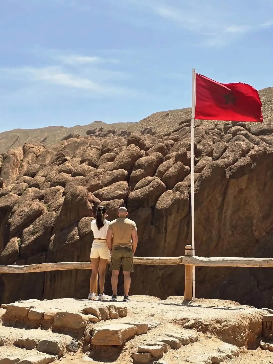 Monkey’s Fingers Hidden Paths: two visitors facing rounded rocks beneath the moroccan flag
