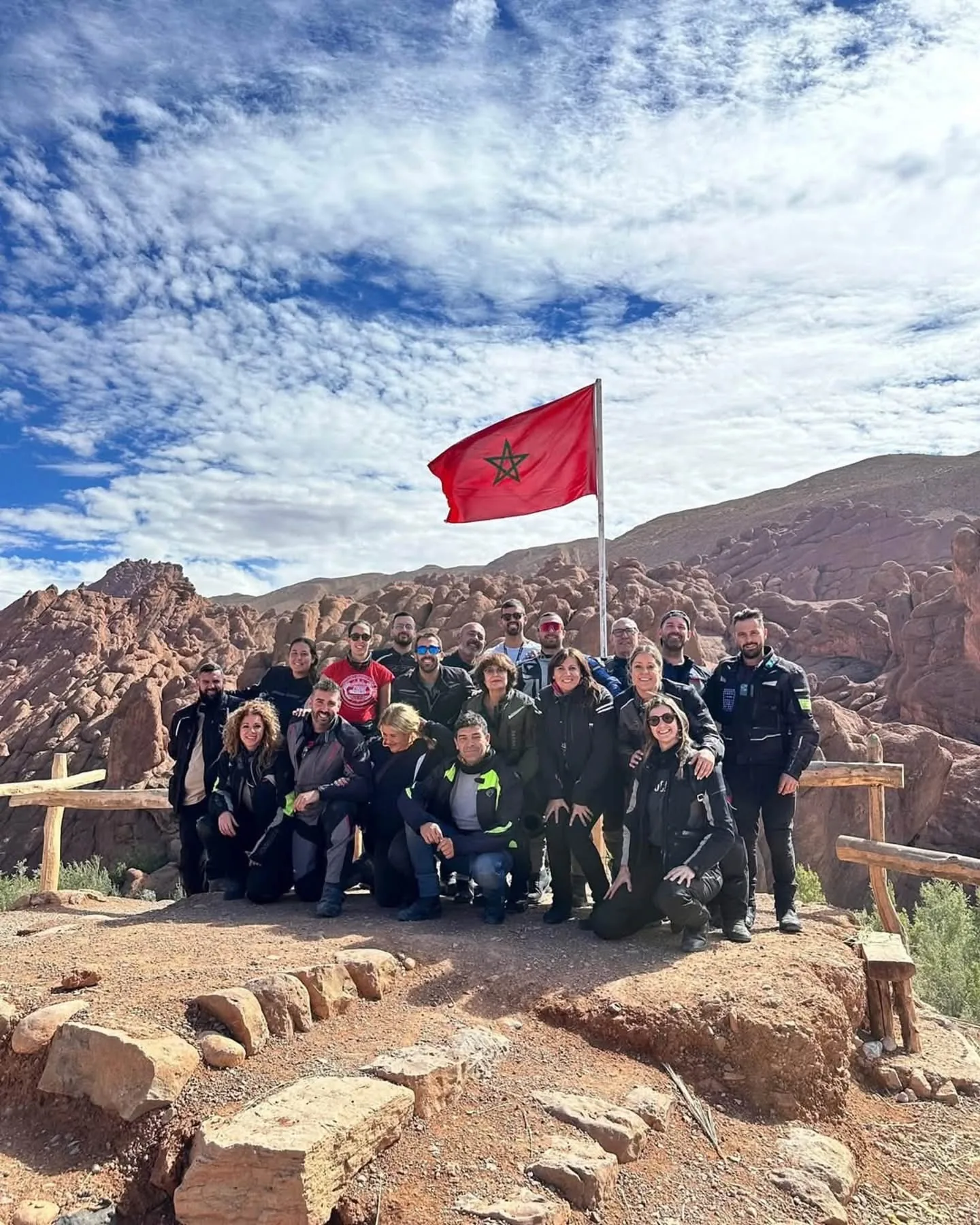 HIKE DADES guests gathered beneath the Moroccan flag among rounded red rocks